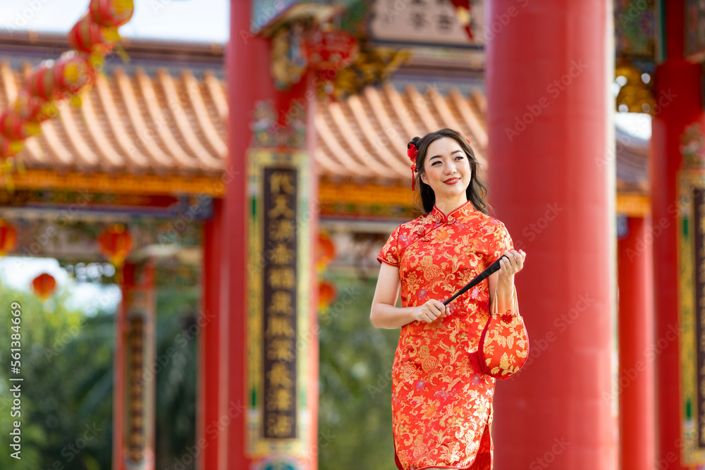 Asian woman in red cheongsam qipao dress holding paper fan while visiting the Chinese Buddhist temple during lunar new year for traditional culture concept