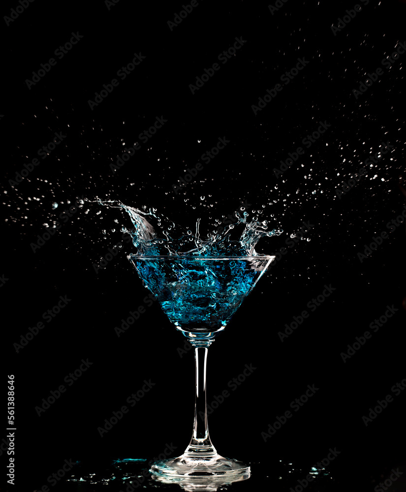 Blue Cocktail Glass with splashing water alcohol, Crystal Cocktail drink splatter splash in air and bubble from glass. Liquor Part freeze shot high speed over black background isolated Blue Cocktail Glass with splashing water alcohol, Crystal Cocktail drink splatter splash in air and bubble from glass. Liquor Part freeze shot high speed over black background isolated