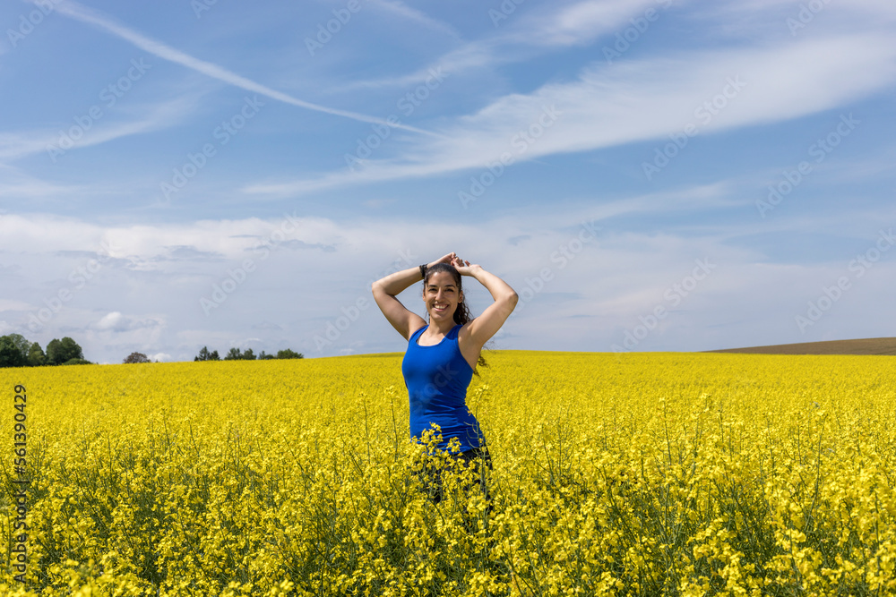 woman portrait and flowers, a dark hair woman in a blue dress is smelling on a canola flower in the middle of a field of canola on a bright summer day woman portrait and flowers, a dark hair woman in a blue dress is smelling on a canola flower in the middle of a field of canola on a bright summer day