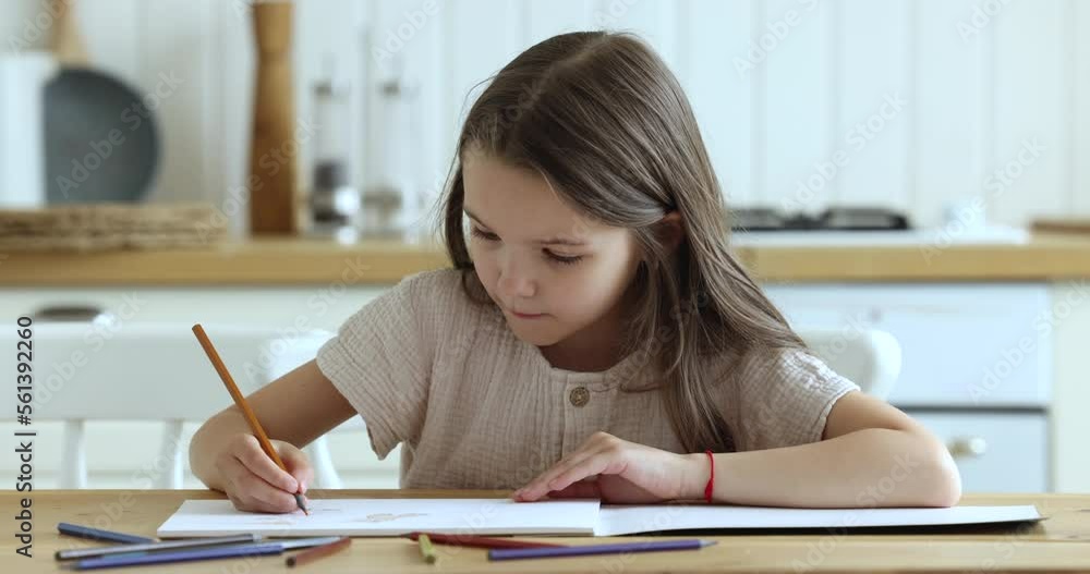 Pretty little girl drawing pictures in paper sketchbook with colored pencils, looks focused and engrossed in creative hobby sit at table in domestic kitchen at home, close up. Pastime of kid at home Pretty little girl drawing pictures in paper sketchbook with colored pencils, looks focused and engrossed in creative hobby sit at table in domestic kitchen at home, close up. Pastime of kid at home