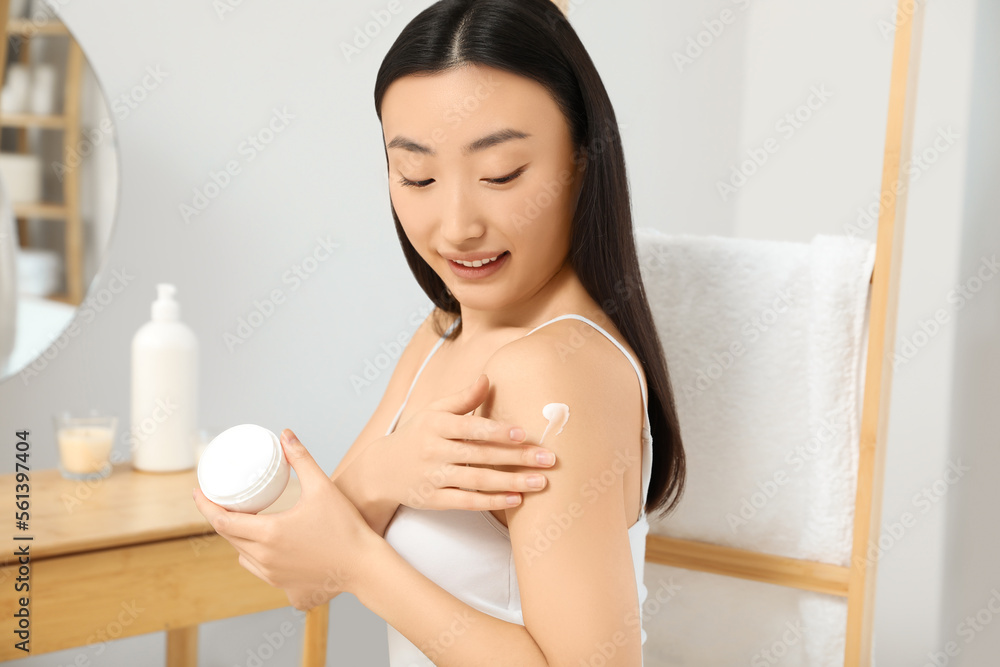Beautiful young Asian woman applying body cream on shoulder in room Beautiful young Asian woman applying body cream on shoulder in room