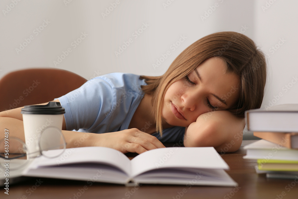Young tired woman sleeping near books at wooden table indoors Young tired woman sleeping near books at wooden table indoors