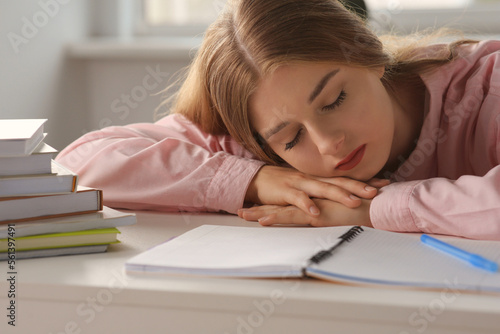 Young tired woman sleeping near books at white table indoors