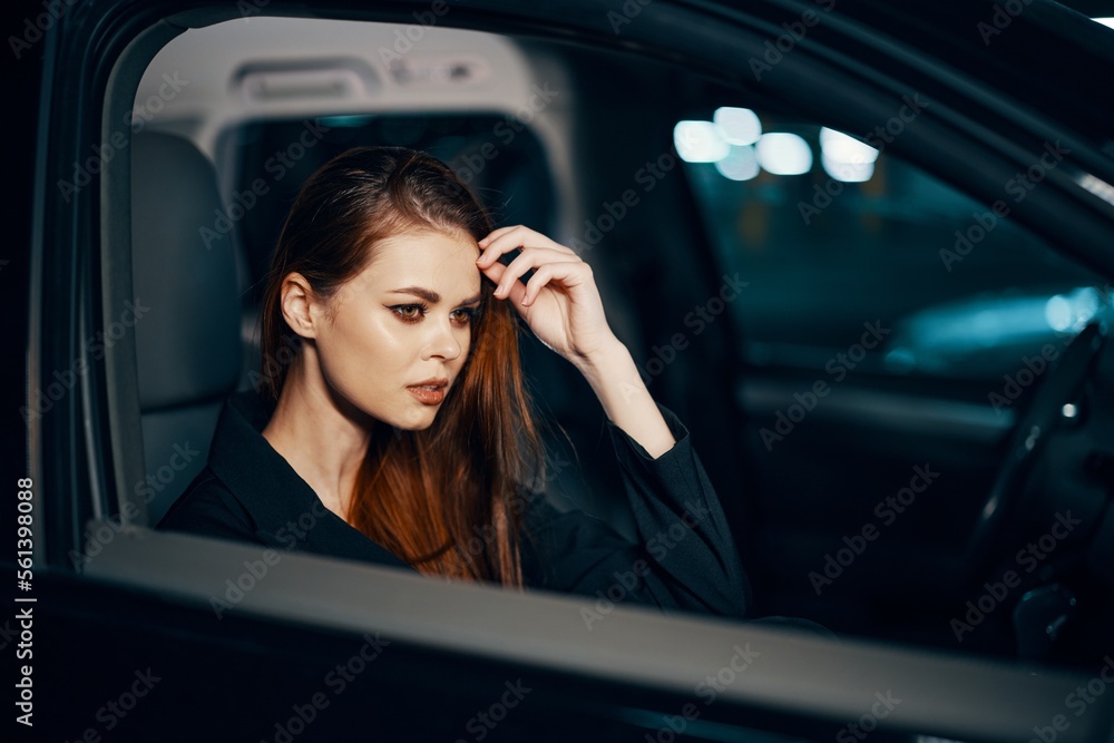 a stylish, luxurious woman is sitting in a black car at night, straightening her long, styled hair