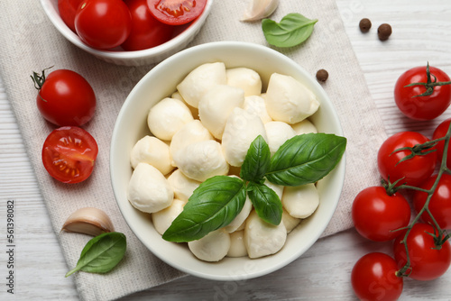 Delicious mozzarella balls in bowl  tomatoes and basil leaves on white wooden table  flat lay