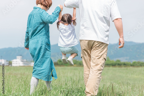 公園を手を繋いでジャンプしながら歩く家族・親子・ファミリーの後ろ姿（子供・両親・旅行）