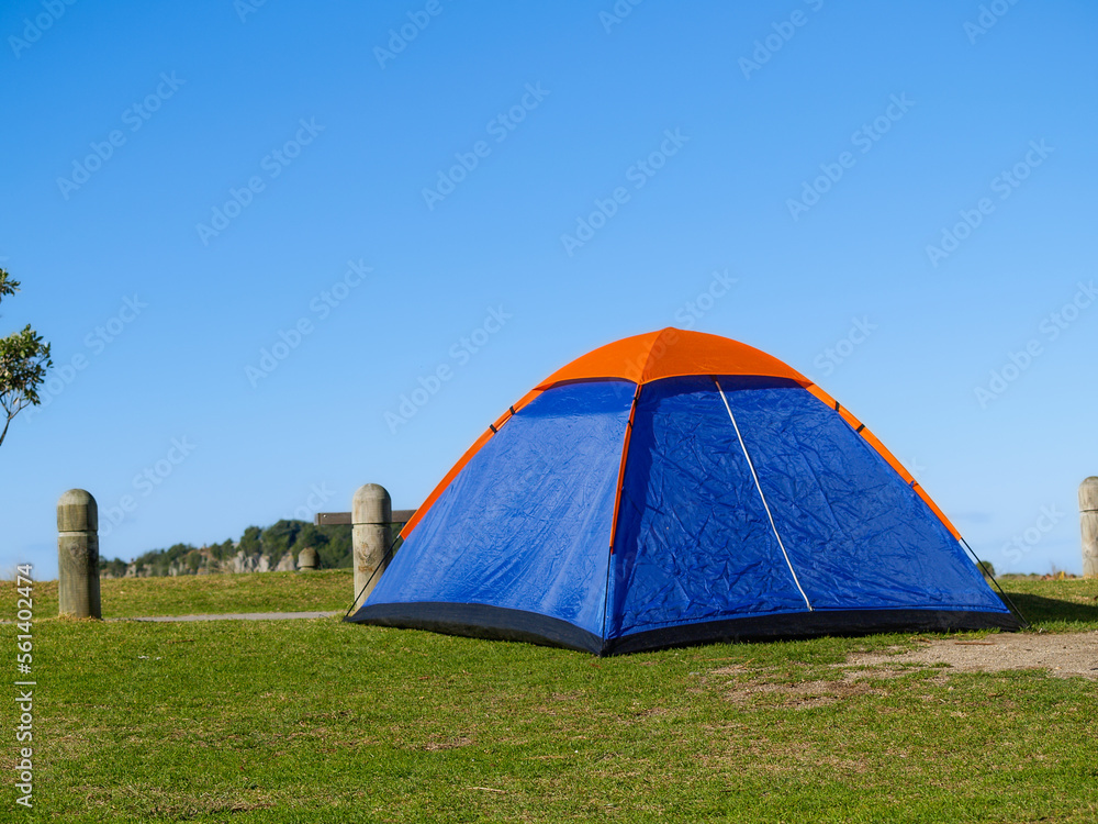 Small blue and orange tent on lawn beside beach