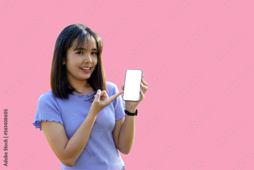 Smiling Asian woman playing and update new applications. Her hand pointed at the phone with blank screen workspace area chatting on pink background. Soft and selective focus. Smiling Asian woman playing and update new applications. Her hand pointed at the phone with blank screen workspace area chatting on pink background. Soft and selective focus.