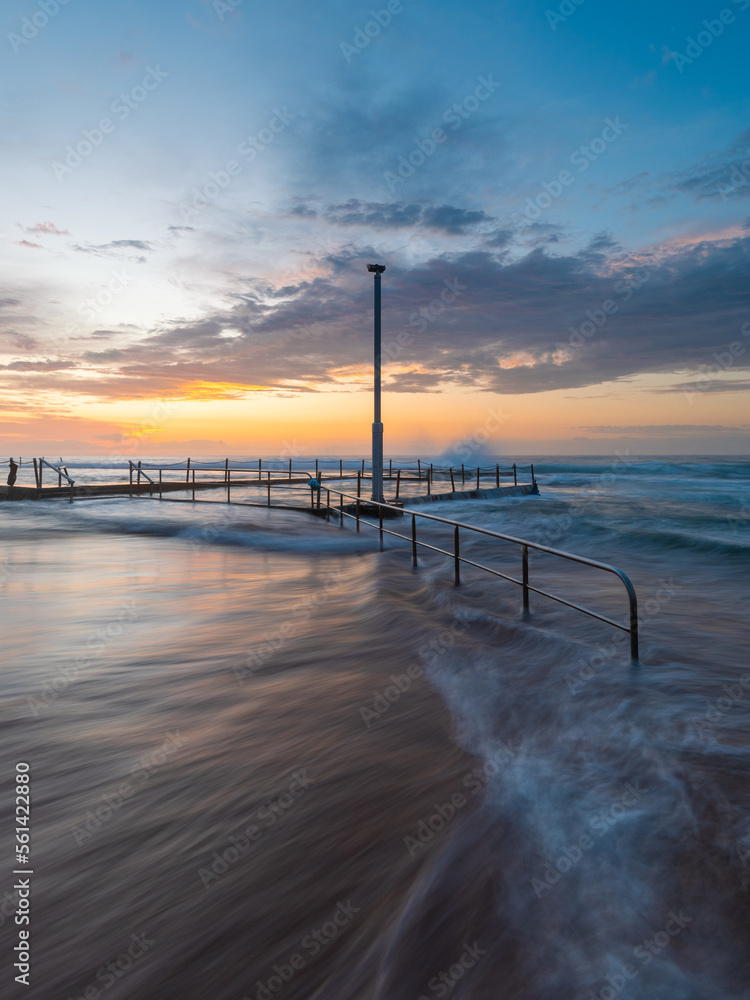 Wave flowing around Mona Vale rock pool in the morning.