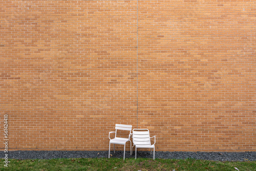 Two empty plastic chairs next to the wall of red bricks