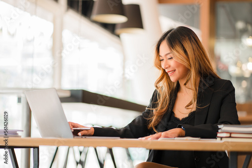 Asian businesswoman working on charts and graphs showing results in office with documents and laptop Worker documents calculating financial indicators, smiling and happy with success.