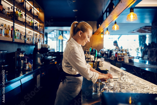 Fotografie A bartender is working with clean glasses behind a counter in a bar