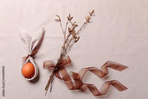 Easter background. Birch branches with brown catkins tied with a transparent ribbon with gold thread. Red egg with bunny ears. Cotton tablecloth. Place for text. photo