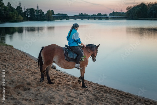 Young beautiful girl on a horse near the river in the evening.