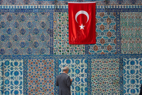 A man prays in front of beautiful Iznik tiles outside the tomb of Abu Ayyub al-Ansari in the Eyup Sultan mosque on the banks of the Golden Horn on the European side of Istanbul, Turkey.. photo