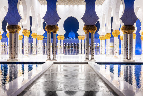 Symmetrical nightshot of the colonnade of the Sheik Zhayed mosque, with a marble catwalk surrounded by water