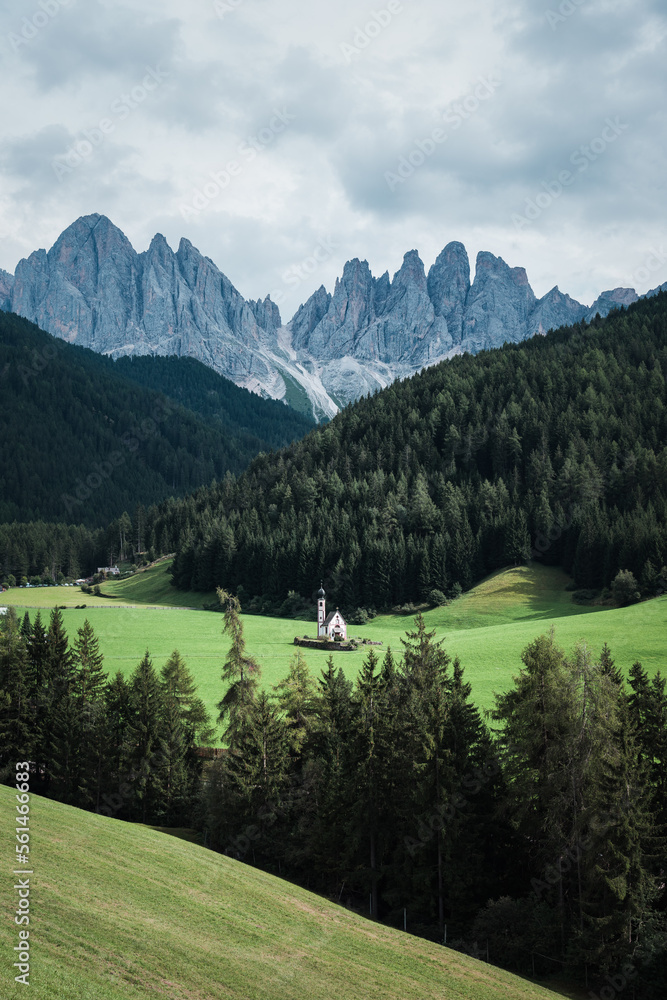 Kleine Kirche auf grüner Wiese in den Dolomiten mit Bergmassiv im Villnöstal mit den Geislerspitzen.