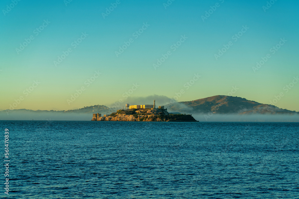 Distant alcatraz insland on the ocean with mist and fog and background mountains in golden sunset or sunrise