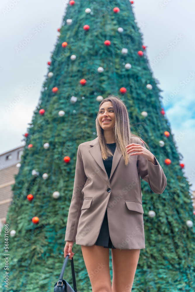 Beautiful christmas tree in the city city, young woman in a trench coat in a fashionable posing Beautiful christmas tree in the city city, young woman in a trench coat in a fashionable posing