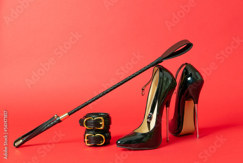 Adult sex games. Kinky lifestyle. Spank and a pair of black high-heeled shoes on the red background. Bdsm outfit photo