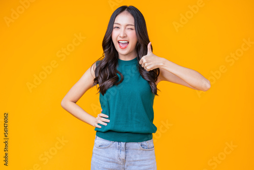 casual happiness asian female woman smiling cheerful in green tshirt blue jean relax peaceful positive thinking carefree lifestyle standing hand gesture face expression with yellow color background 