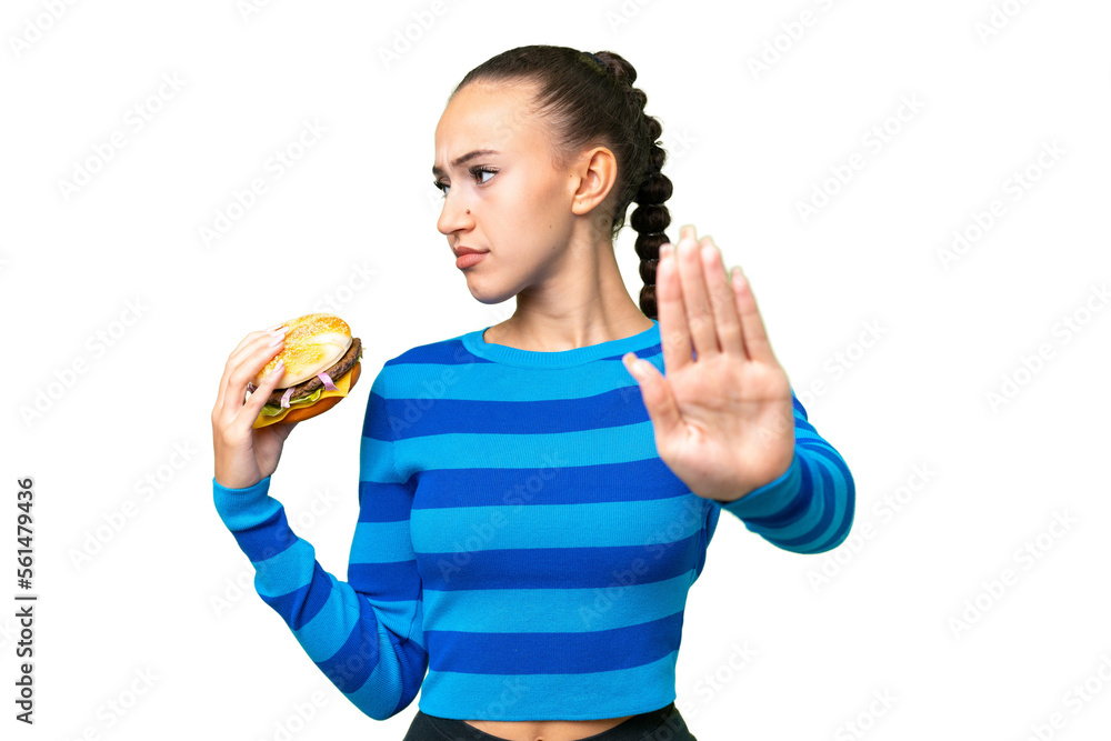 Young Arab woman holding a burger over isolated background making stop gesture and disappointed Young Arab woman holding a burger over isolated background making stop gesture and disappointed