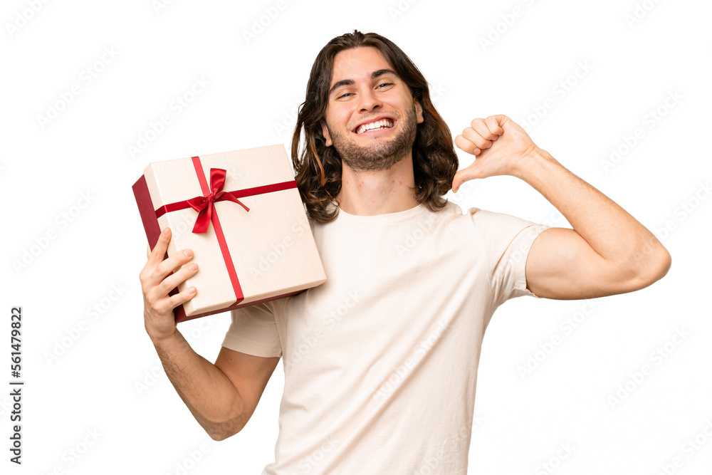 Young handsome man holding a gift over isolated background proud and self-satisfied Young handsome man holding a gift over isolated background proud and self-satisfied