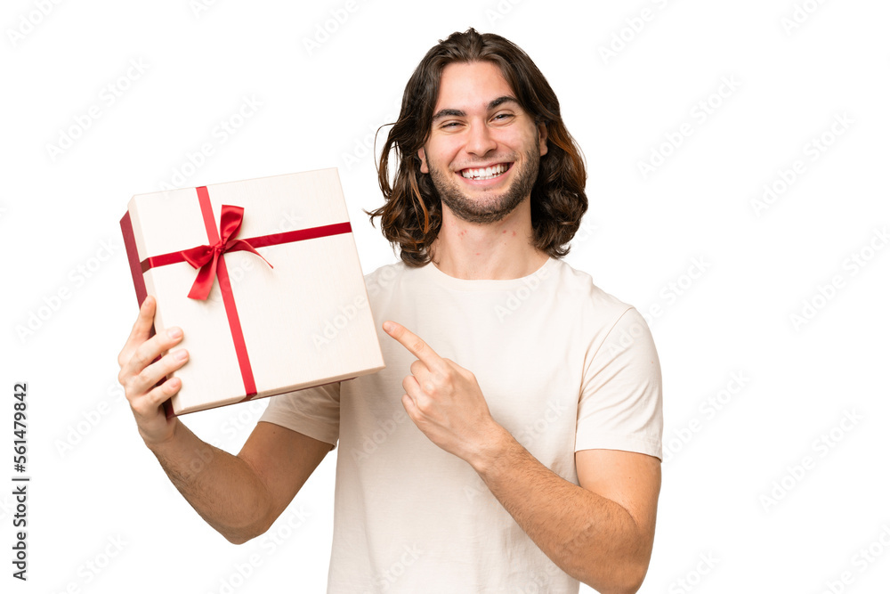 Young handsome man holding a gift over isolated background and pointing it Young handsome man holding a gift over isolated background and pointing it
