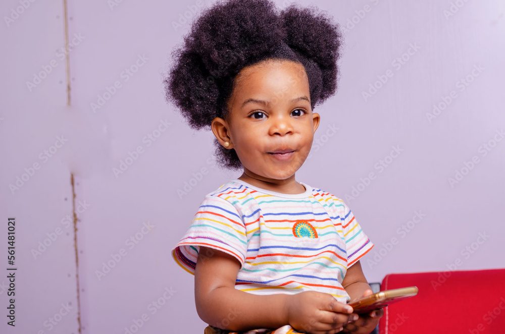 Fototapeta premium Curious little girl playing games on her mobile phone indoors.