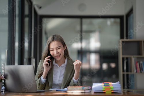 Successful confident beautiful Asian businesswoman, business leader, and manager working at the office, talking on the phone with friends or colleagues, looking away, smiling