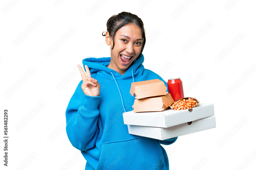 Young Uruguayan woman holding pizzas and burgers over isolated chroma key background smiling and showing victory sign Young Uruguayan woman holding pizzas and burgers over isolated chroma key background smiling and showing victory sign