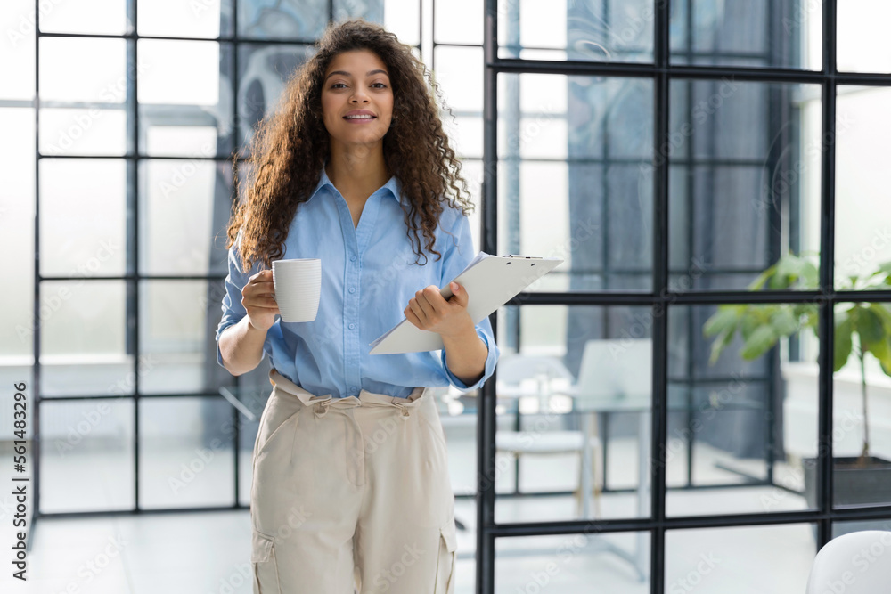 Businesswoman standing in the office corridor with documents and coffee. Businesswoman standing in the office corridor with documents and coffee.