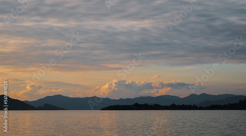 Gorgeous sunset sky with clouds over the sea. Silhouettes of a range of islands and mountains on the horizon. Idea for backgrounds or screens. Dramatic sunset, beauty of nature, vacation time