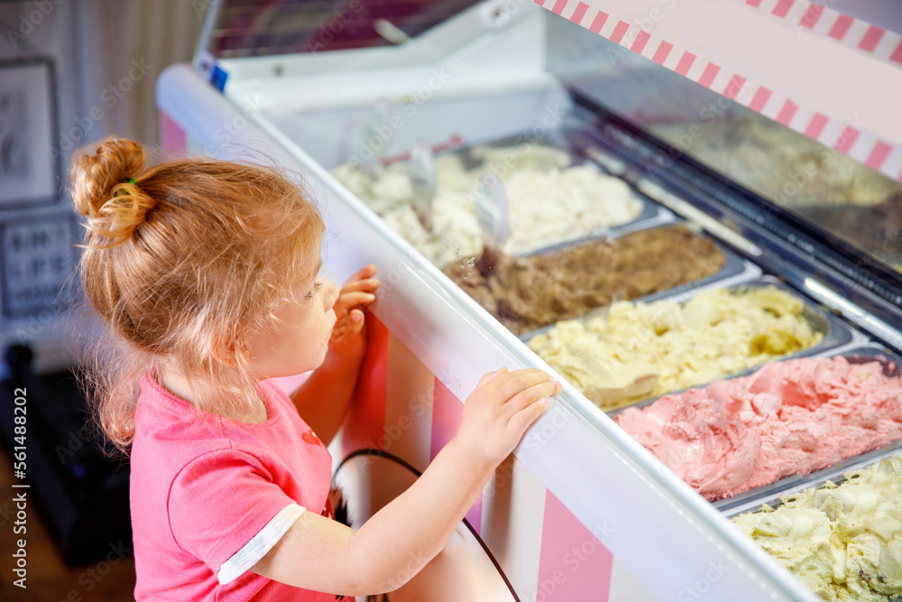 Cute little toddler girl choosing and buying ice cream in a cafe. Happy baby child looking at different sorts of icecream. Sweet home made dessert Cute little toddler girl choosing and buying ice cream in a cafe. Happy baby child looking at different sorts of icecream. Sweet home made dessert