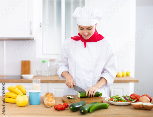 Proffesional woman cook in white uniform chopping vegetables