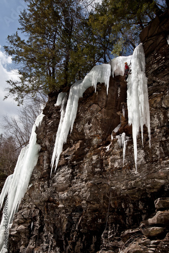 A climber ascends a radically overhanging rock face to reach the ice daggers above on a steep mixed rock and ice route in the Devils Kitchen section of the Catskill mountains, near photo