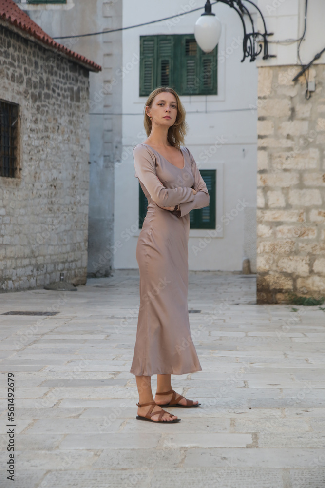 Fashionable tourist woman in silk beige dress in the streets of Old town of Sibenik, Croatia