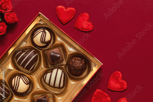 Gift box with chocolate candies and red heart decoration for Valentine's Day on a burgundy background. Top view. Copy space.