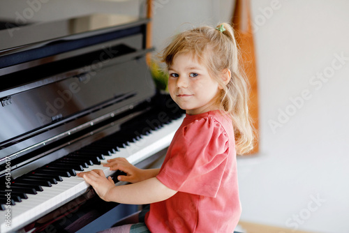 Beautiful little toddler girl playing piano in living room. Cute preschool child having fun with learning to play music instrument. Early musical education for children.