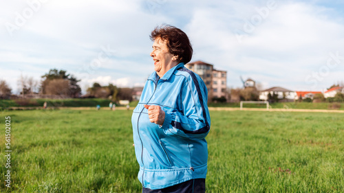 Running and sports activity. An elderly smiling woman in sports clothes runs through a green field. Side view. The concept of the International Day of Older Persons © _KUBE_
