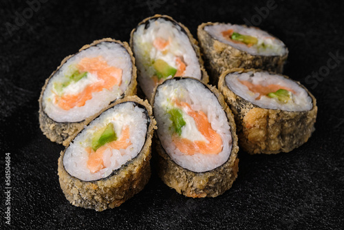 baked sushi rolls with salmon and avocado on black concrete background