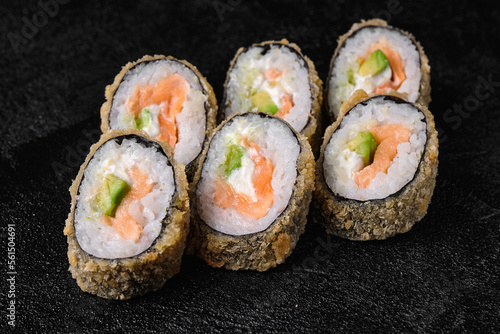 baked sushi rolls with salmon and avocado on black concrete background