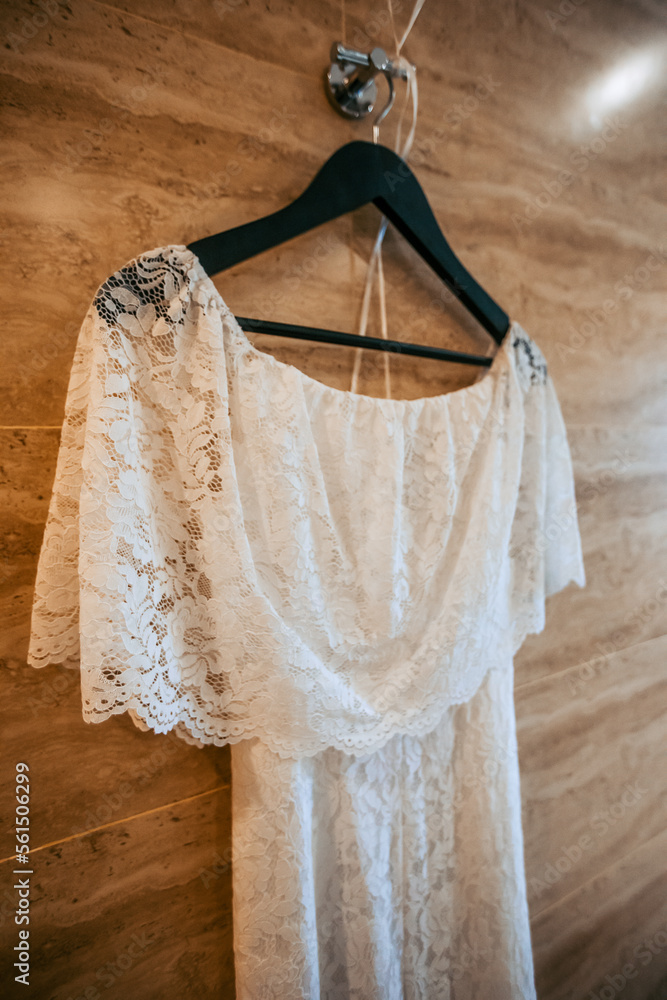 Beautiful white wedding dress hangs on a hanger indoors. Close-up photo, bride morning. Beautiful white wedding dress hangs on a hanger indoors. Close-up photo, bride morning.
