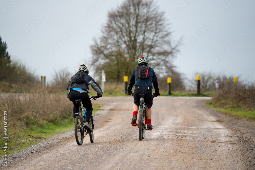 a pair of casual cyclists riding along across a country mud track a pair of casual cyclists riding along across a country mud track