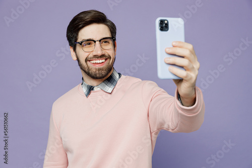 Young smiling IT man he wear casual clothes pink sweater glasses doing selfie shot on mobile cell phone post photo on social network isolated on plain pastel light purple background studio portrait. © ViDi Studio