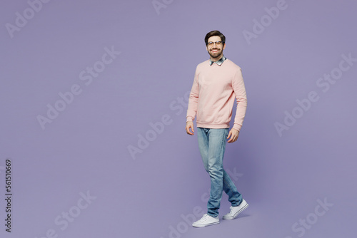 Full body sideways happy fun young caucasian IT man he wears casual clothes pink sweater glasses walking going strolling look camera isolated on plain pastel light purple background studio portrait.