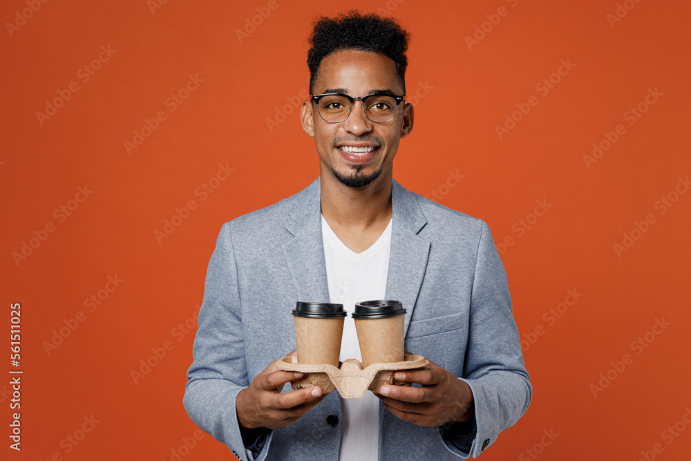 Young employee business man corporate lawyer in classic formal grey suit shirt glasses work in office hold takeaway delivery craft paper brown cup coffee to go isolated on plain red orange background. Young employee business man corporate lawyer in classic formal grey suit shirt glasses work in office hold takeaway delivery craft paper brown cup coffee to go isolated on plain red orange background.