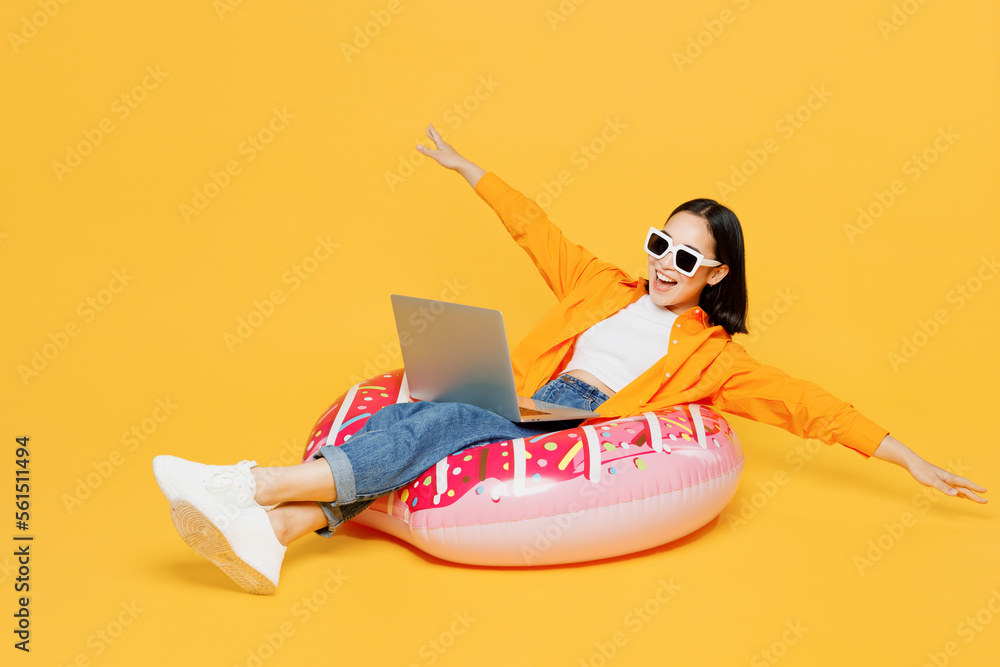Young woman in summer clothes sit rubber ring use laptop pc computer spread hands isolated on plain yellow background. Tourist travel abroad in free time rest getaway Air flight trip journey concept Young woman in summer clothes sit rubber ring use laptop pc computer spread hands isolated on plain yellow background. Tourist travel abroad in free time rest getaway Air flight trip journey concept