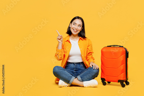 Young woman in summer casual clothes sit near suitcase point aside on area isolated on plain yellow background. Tourist travel abroad in free spare time rest getaway. Air flight trip journey concept #561511444