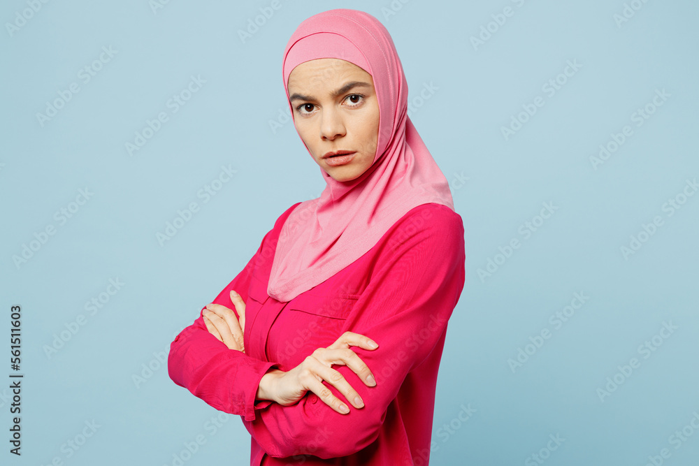 Fototapeta premium Young sad shrewd arabian muslim woman in pink abaya hijab hold hands crossed folded look camera isolated on plain pastel light blue cyan background studio portrait People uae islam religious concept